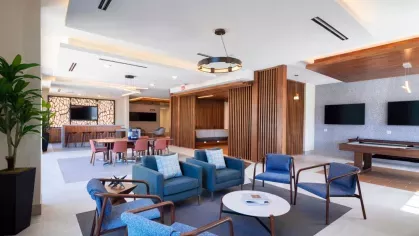 The Everly's stylish resident lounge, featuring plush blue seating, a pool table, multiple TVs, and a co-working space with contemporary wood paneling.