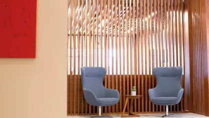 A cozy nook with two blue accent chairs and a small wooden table, framed by warm wooden slats and soft lighting for a private conversation area.