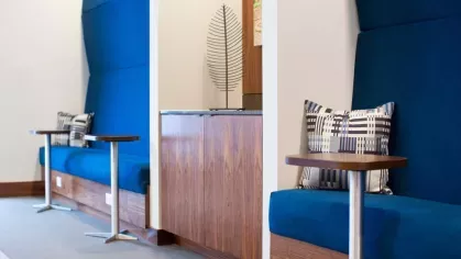 A modern work lounge with deep blue upholstered booths, individual side tables, and contemporary pillows, creating a stylish yet functional workspace.