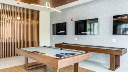 A luxury game room with a wooden pool table, sleek pendant lighting, and multiple TVs, providing an upscale entertainment experience.