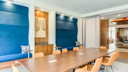 A stylish conference room with a long wooden table, plush seating, and blue accent walls, designed for productive meetings or work-from-home sessions.