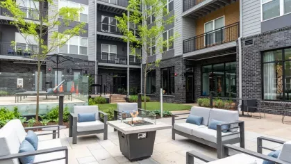 An inviting outdoor courtyard with a fire pit, modern lounge seating, and lush greenery, creating the perfect space for socializing and unwinding.