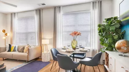A beautifully set dining table with plush blue chairs, positioned next to a contemporary kitchen with wood-finish cabinets and stainless-steel appliances.