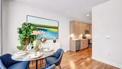 A beautifully set dining table with plush blue chairs, positioned next to a contemporary kitchen with wood-finish cabinets and stainless-steel appliances.
