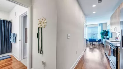 A sleek hallway with hardwood flooring leading to a modern kitchen and a bathroom with soft blue accents.