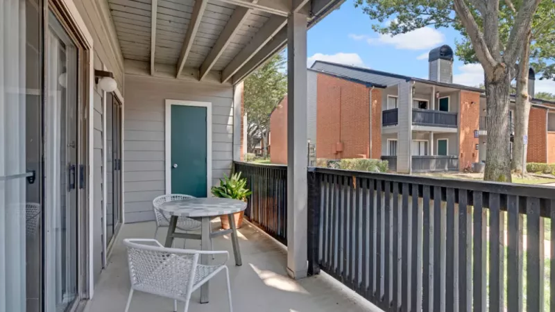 Covered balcony with a small white table, two chairs, and views of the red brick apartment buildings.