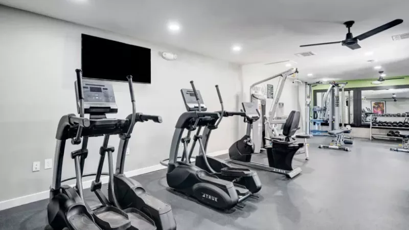 Gym with cardio equipment, including ellipticals and a stationary bike, against a backdrop of large mirrors.