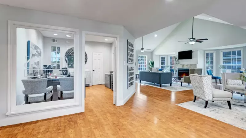 Spacious clubhouse with wood flooring, a fireplace, and comfortable seating areas for residents.