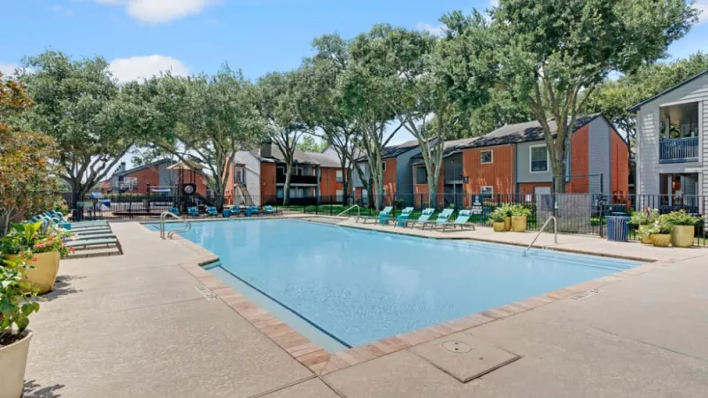 Large outdoor pool surrounded by red brick apartment buildings and lush trees.