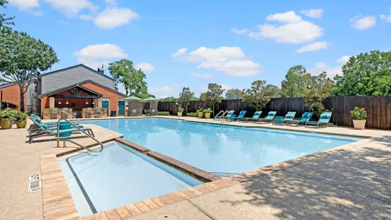 Sparkling swimming pool with lounge chairs and shaded seating areas surrounded by greenery.