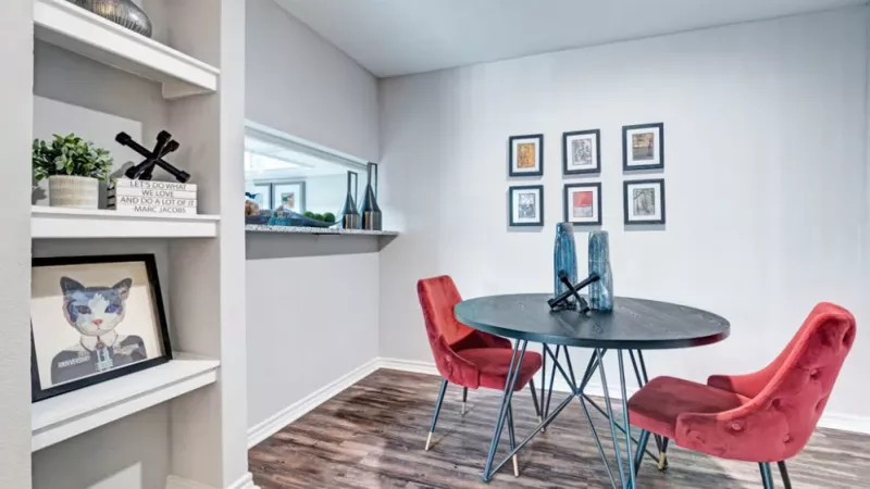 Cozy dining area with a black round table, red velvet chairs, and built-in shelving displaying decor.