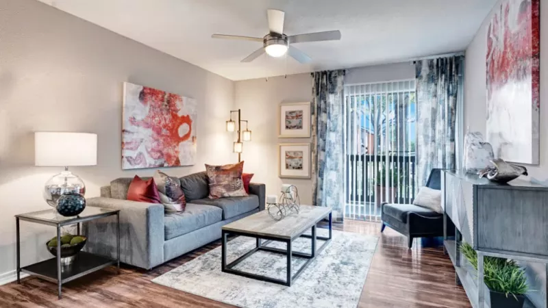 Stylish living room with contemporary decor, abstract art, and a balcony view through vertical blinds.
