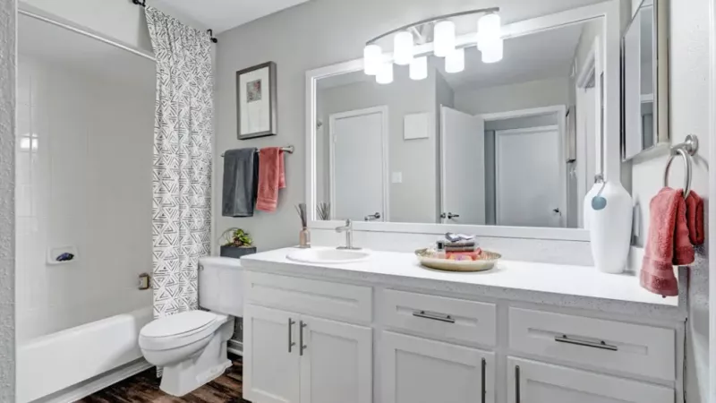 Bright bathroom with white cabinetry, a large mirror, and a shower-tub combo with a geometric patterned curtain.