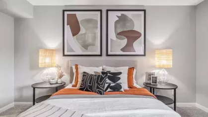 Bedroom with warm tones, abstract art above the bed, and bedside lamps on black tables.