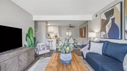 Open-concept living room featuring a blue couch, wooden coffee table, and a TV on a rustic console.
