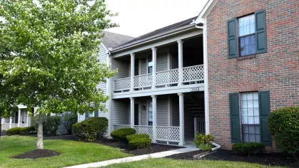 A two-story apartment building with a mix of brick and gray siding surrounded by lush landscaping.