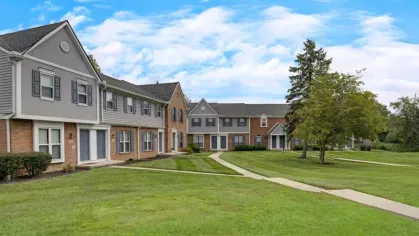 Spacious green lawns in front of a row of classic brick and gray townhouse buildings.