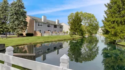 A peaceful canal lined with greenery and apartment buildings, with clear water reflecting the scenery.