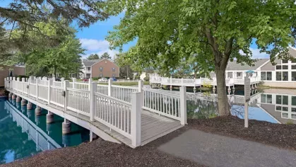 A white wooden bridge over a serene waterway leading to a community clubhouse.