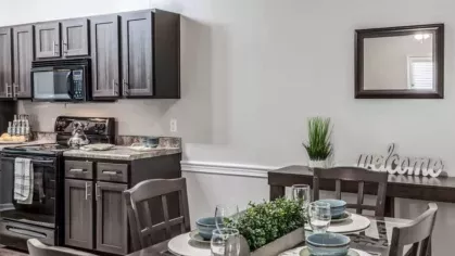Elegant dining area with dark wood furniture, set for four, adjacent to a modern kitchen with black appliances.