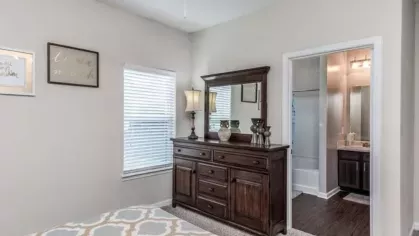 Master bedroom with a classic wooden dresser, mirror, and access to an en-suite bathroom, showcasing luxury apartment living.