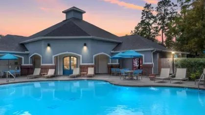Inviting swimming pool at The Landings of Conroe at sunset, with a beautifully lit clubhouse, poolside seating, and vibrant blue sky with soft pink clouds.