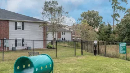 Fenced dog park with agility tunnel and open lawn area at The Landings of Conroe, providing a safe and fun environment for pets.