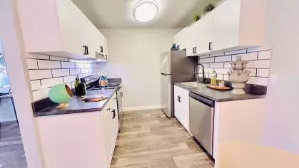 Spacious kitchen with white cabinets, stainless steel appliances, subway tile backsplash, and wood-style flooring, creating a clean and modern atmosphere.