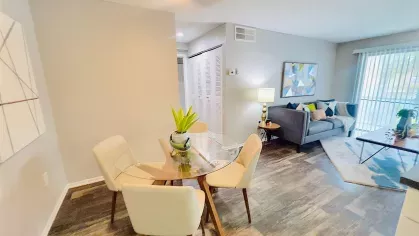 Stylish dining area with a round glass table and cream-colored chairs, accented by modern geometric artwork on the wall, located adjacent to a well-equipped kitchen for a seamless open-concept living space.