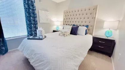 Cozy bedroom with a tufted headboard, white bedding, and vibrant blue accent decor.
