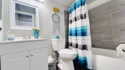 Contemporary bathroom with a white vanity, framed mirror, modern lighting, and a shower-tub combination with stylish gray tile, accented by a blue-and-white shower curtain.