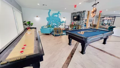 Spacious and modern community lounge featuring a pool table, seating areas, large windows, and a vibrant teal accent wall, creating a lively and inviting space for social activities.