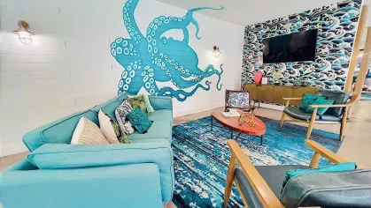 A welcoming seating area featuring mid-century modern chairs with wooden frames, a textured blue area rug, and a natural wood coffee table, positioned near sleek sliding glass doors that open to an adjacent space, blending comfort with contemporary design.