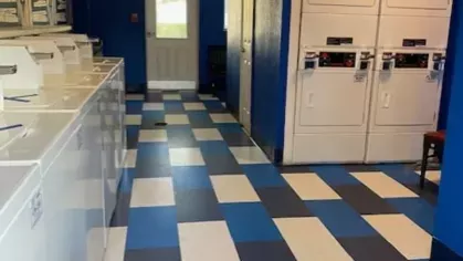 Bright and clean laundry facility with rows of washers and dryers, complemented by a bold blue and white checkered floor design.
