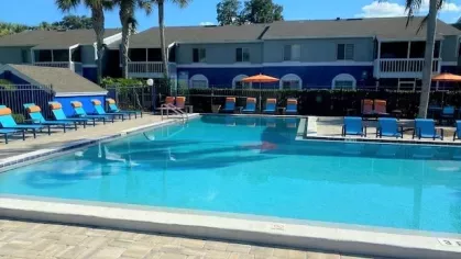 Sparkling outdoor pool surrounded by colorful lounge chairs, orange umbrellas, and tropical palm trees, offering a perfect spot for relaxation under the sun.