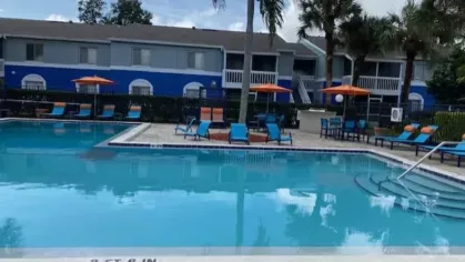 Sparkling outdoor pool surrounded by blue lounge chairs, palm trees, and vibrant orange umbrellas.