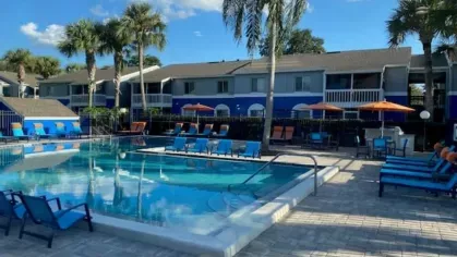 Outdoor pool area highlighted during the golden hour, featuring lounge chairs and vibrant umbrellas against a serene backdrop of palm trees and modern apartments.