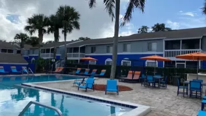 A spacious pool area with palm trees, lounge chairs, and seating options, showcasing a resort-style atmosphere ideal for leisure and socializing.