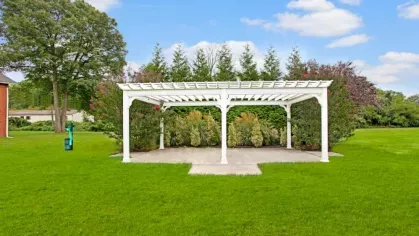 A white pergola set against lush green landscaping and a clear blue sky.