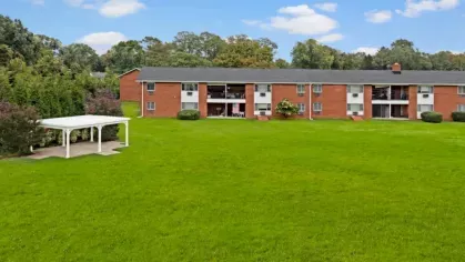 Expansive green lawn with a red-brick apartment building and a white pergola in the background.