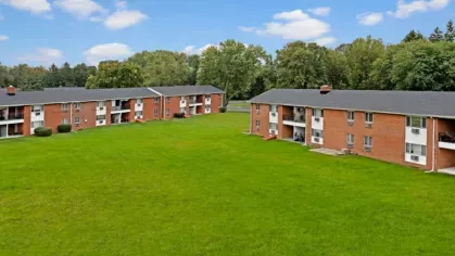 Two red-brick apartment buildings with a large, well-maintained green lawn in between.