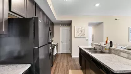 Modern kitchen featuring dark wood cabinetry, black appliances, and a marble-look countertop with a breakfast bar at Lawndale Commons Palm Luxury Apartments.