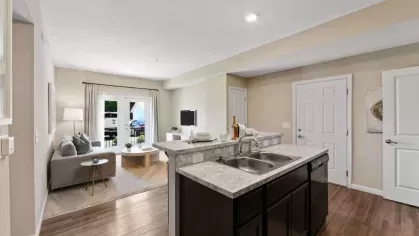 Open-concept kitchen and living area with a bright interior, featuring a spacious countertop, a cozy sofa, and a large window leading to a balcony.