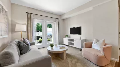 Elegant living space with a soft-toned sofa, accent pillows, and a modern entertainment setup, leading to a private patio.
