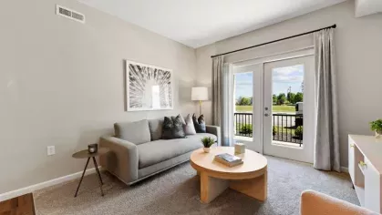 Bright and spacious living area featuring a neutral color palette, a glass door to a private balcony, and stylish furnishings.