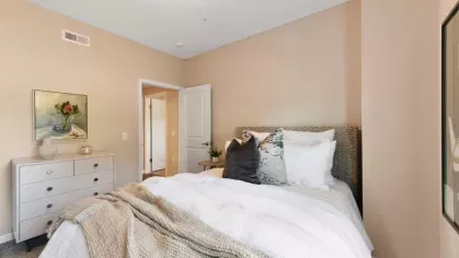 Serene bedroom with warm decor, featuring a rattan headboard, soft linens, and a contemporary dresser.