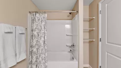 A bright and elegant bathroom with a full-size bathtub, floral-patterned shower curtain, and built-in storage shelves.