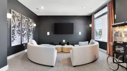 A cozy movie room with modern décor, featuring a large flat-screen TV, curved sofas, and a vintage popcorn cart.