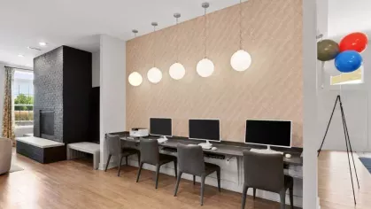 A stylish coworking space at Lawndale Commons, featuring a black fireplace, built-in bench seating, and sleek computer desks with modern lighting.