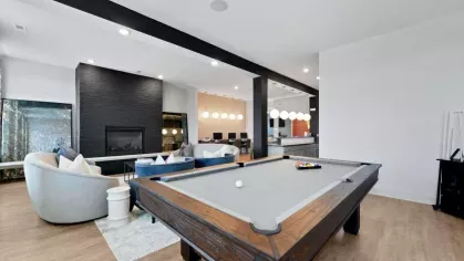 A pool table in the clubhouse of Lawndale Commons, surrounded by modern lounge seating and a fireplace, creating a vibrant social hub.